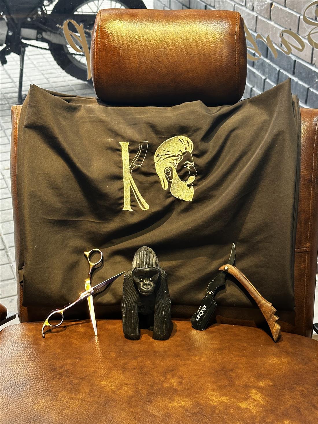 Capa de KingsMen con la K bordada, tijeras y navaja sobre la silla de cuero