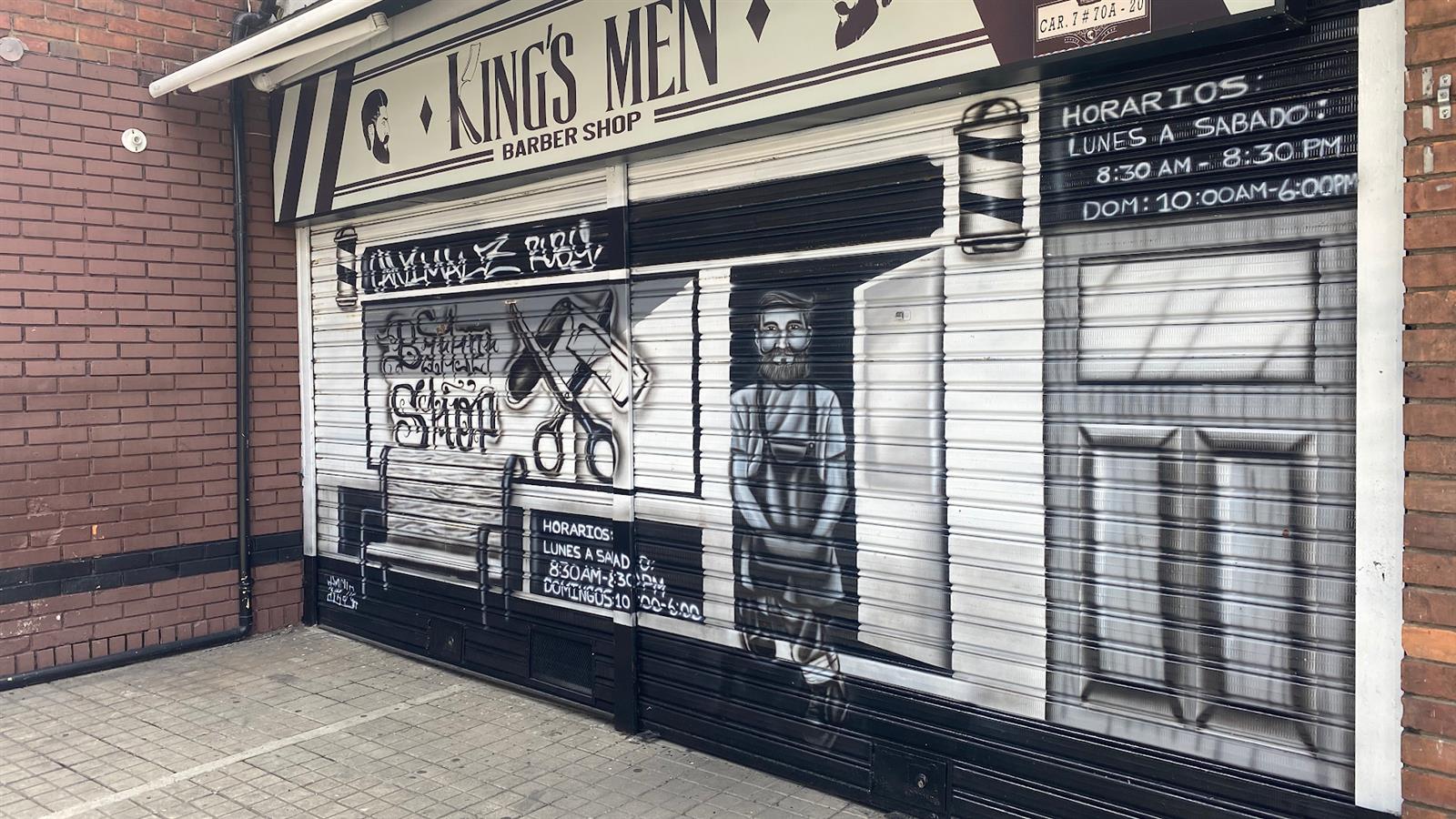 Cortina metálica de KingsMen pintada con un mural de barbería y el horario